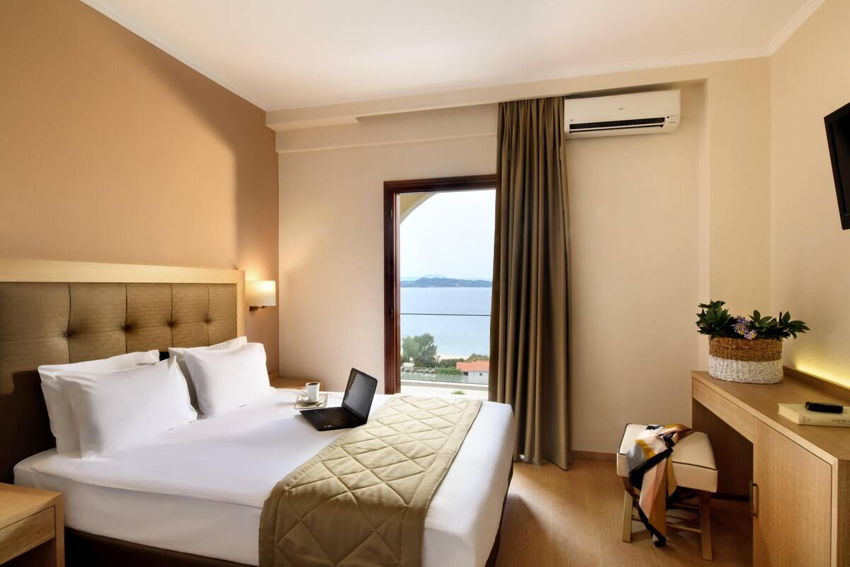 Ein Hotelzimmer mit Bett, Schreibtisch, Laptop, Tasse und Blick aufs Meer.