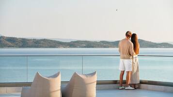 Una pareja de pie en un balcón con vista a un cuerpo de agua y colinas al fondo.