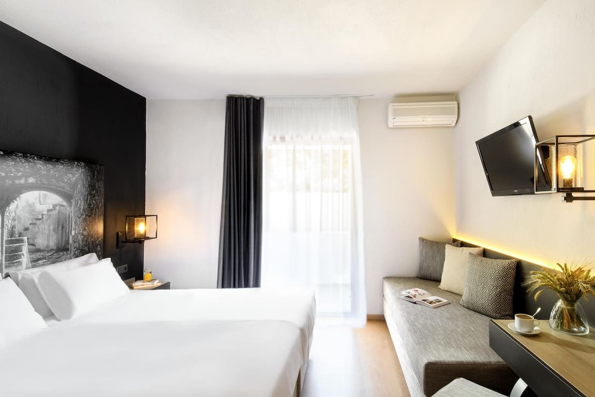 Ein modernes Hotelzimmer mit einem großen Bett, einer Couch, einem Flachbildfernseher und einer Wand-Klimaanlage.