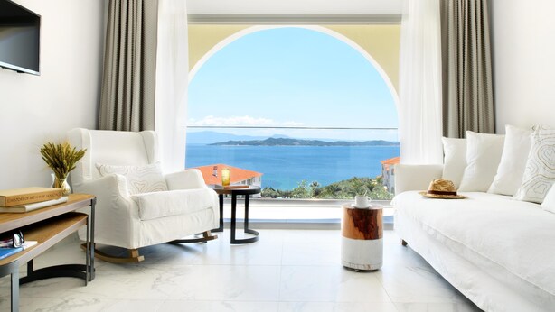 Sala de estar moderna com uma grande janela, móveis brancos, uma mesa pequena e vista para o mar.