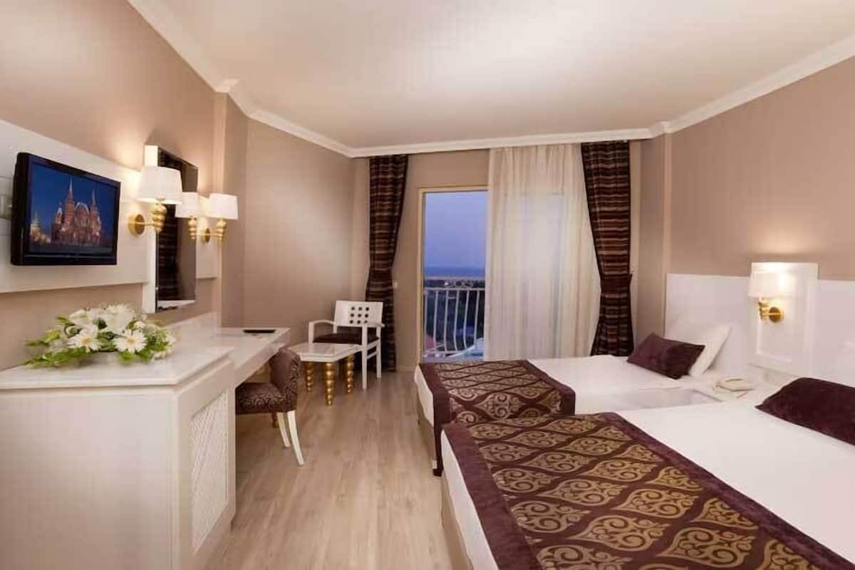 Habitación de hotel con dos camas, un escritorio, una silla y vistas al exterior.