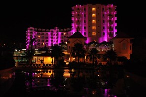 A hotel with multiple floors, a pool area, and a reflection in the water. - Serenis Hotel - All Inclusive (Manavgat)