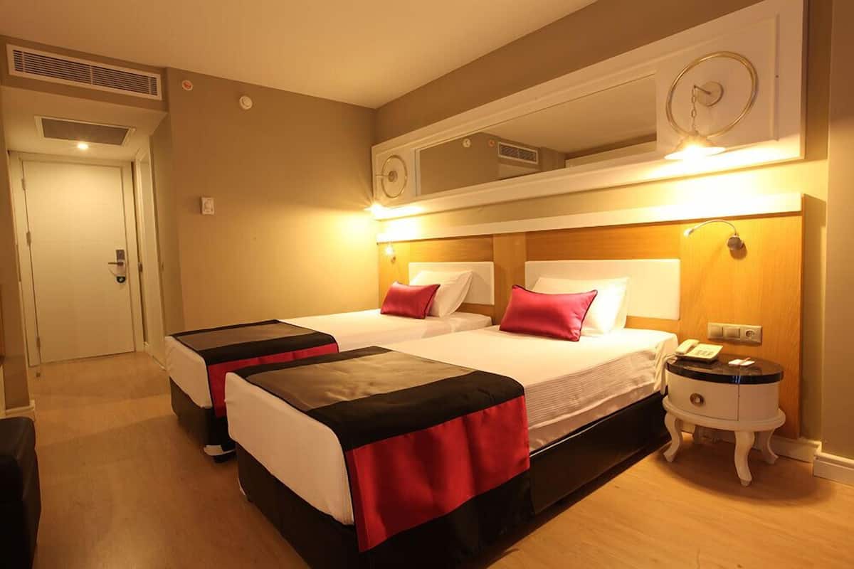 Habitación de hotel con dos camas, una mesita de noche con teléfono y un espejo sobre las camas.