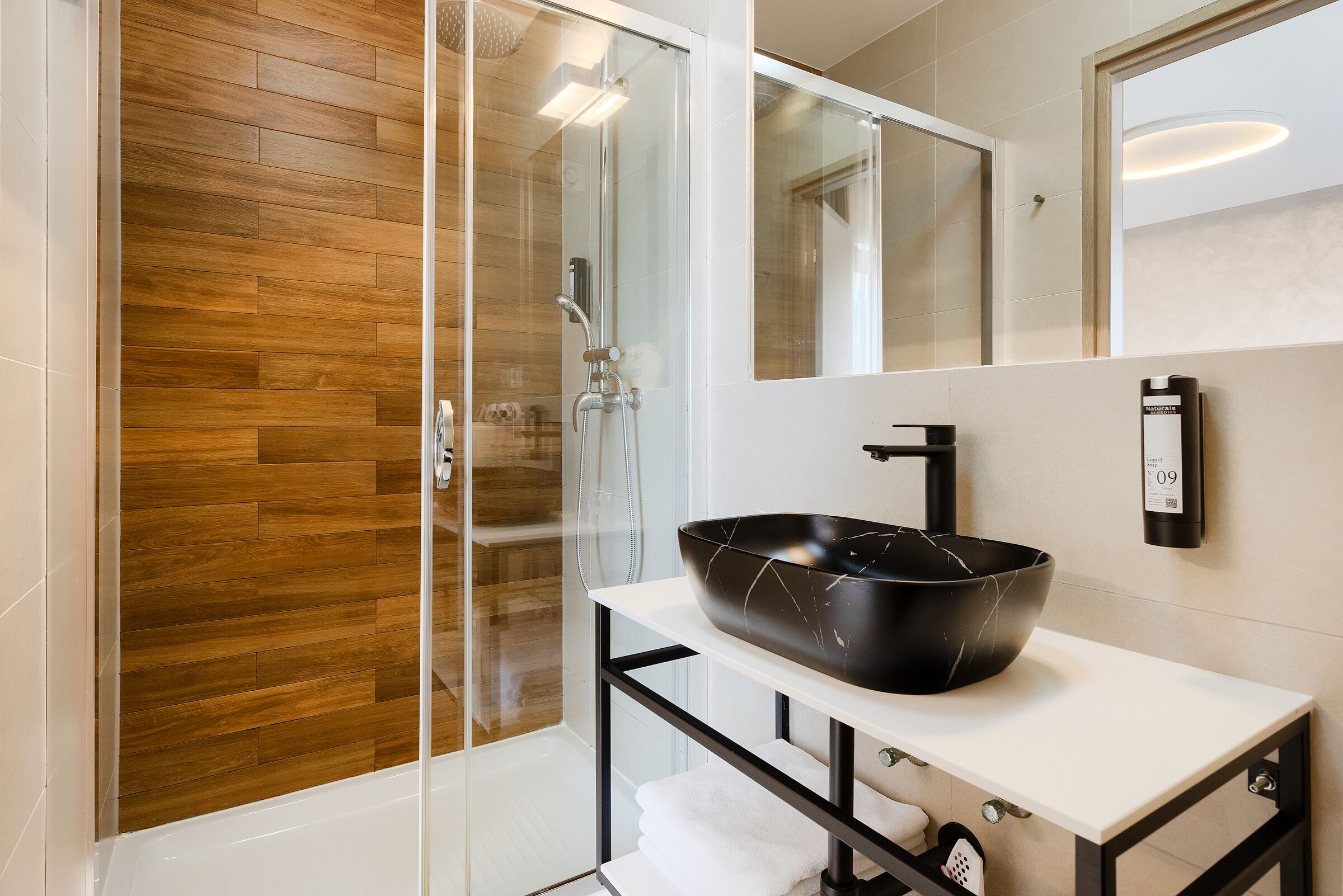 A modern bathroom with a glass-enclosed shower, a black vessel sink, and a white vanity with a mirror.