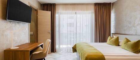 A hotel room with a bed, a desk, a chair, a television, and a large window with curtains.