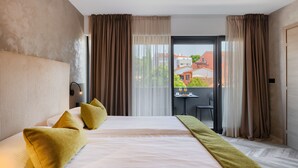 Une chambre d’hôtel avec un grand lit, une vue sur la ville depuis la fenêtre et un balcon équipé d’une table et de chaises.