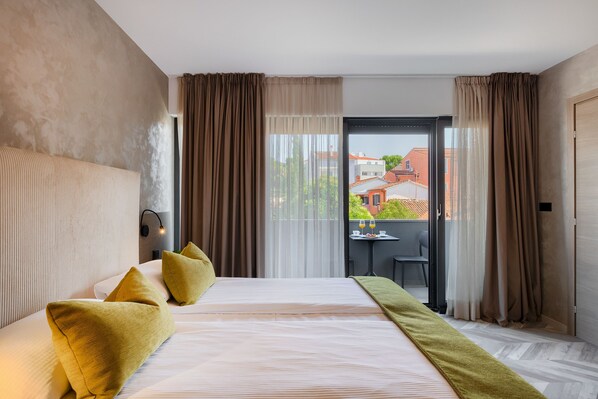 A hotel room with a large bed, a view of the city through the window, and a balcony with a table and chairs.