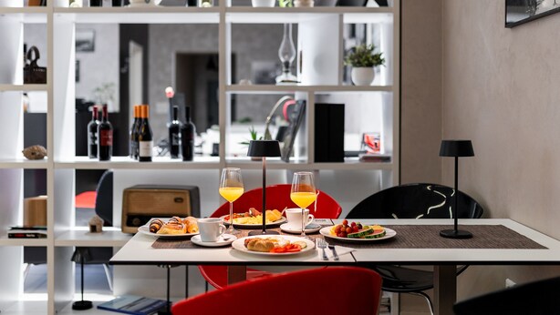 Un coin repas avec une table mise pour le petit-déjeuner, comprenant des assiettes de nourriture, des verres de jus d’orange et une lampe.