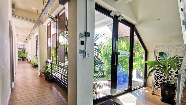 A modern hotel lobby with a wooden floor, a welcome mat, and a glass door leading to an outdoor area with plants. - 26 Bed and Coffee (Chonburi)