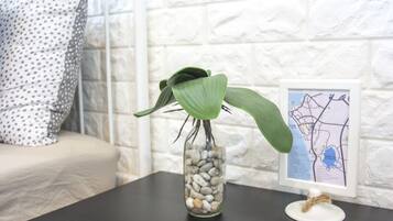 A glass vase with a plant on a dark surface, a white pillow with black dots, and a framed map on a white brick wall.