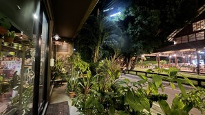 An outdoor seating area with potted plants and a pathway leading to a building entrance. - 26 Bed and Coffee (Chonburi)