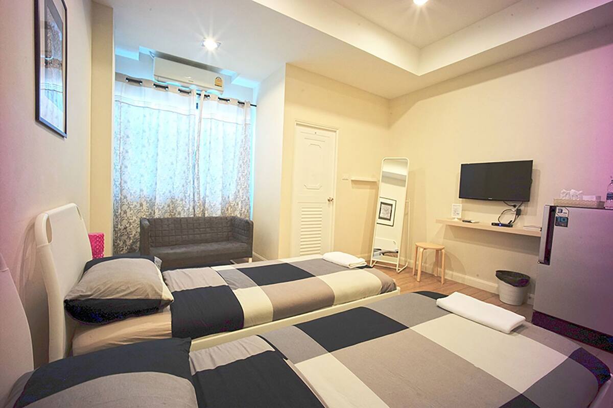 Habitación de hotel con dos camas, un sofá, un televisor, un espejo y una mesita.