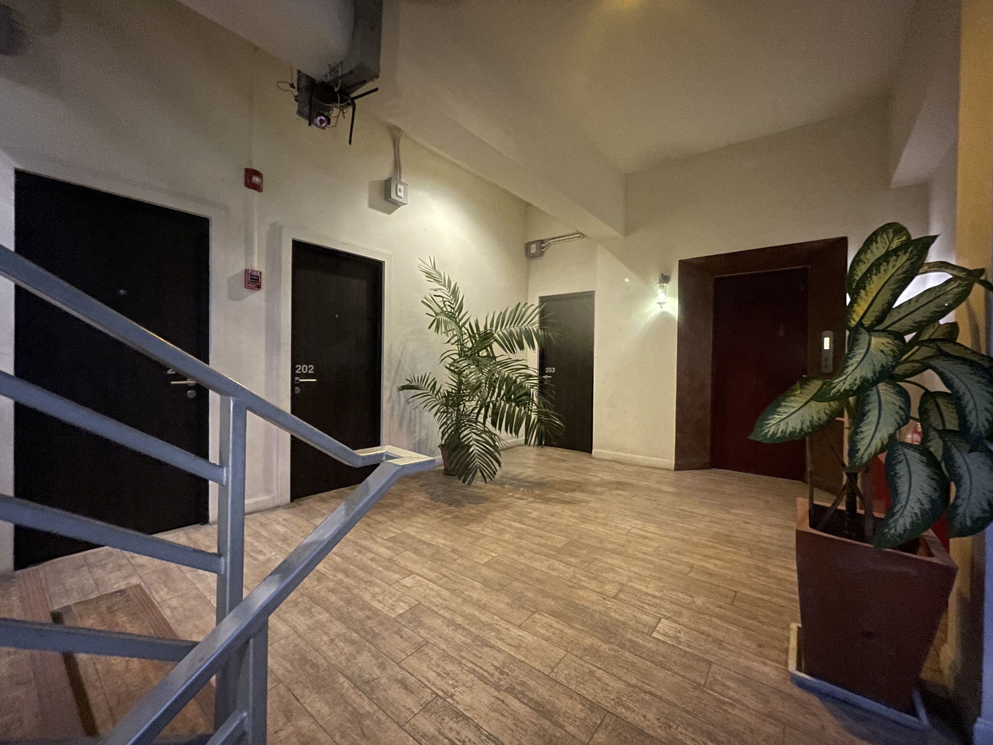 A spacious hallway with wooden flooring, black doors, and a staircase with a metal railing.
