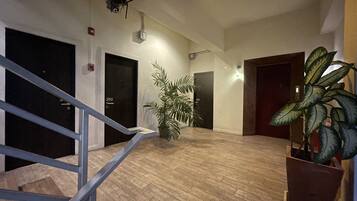 A spacious hallway with wooden flooring, black doors, and a staircase with a metal railing.
