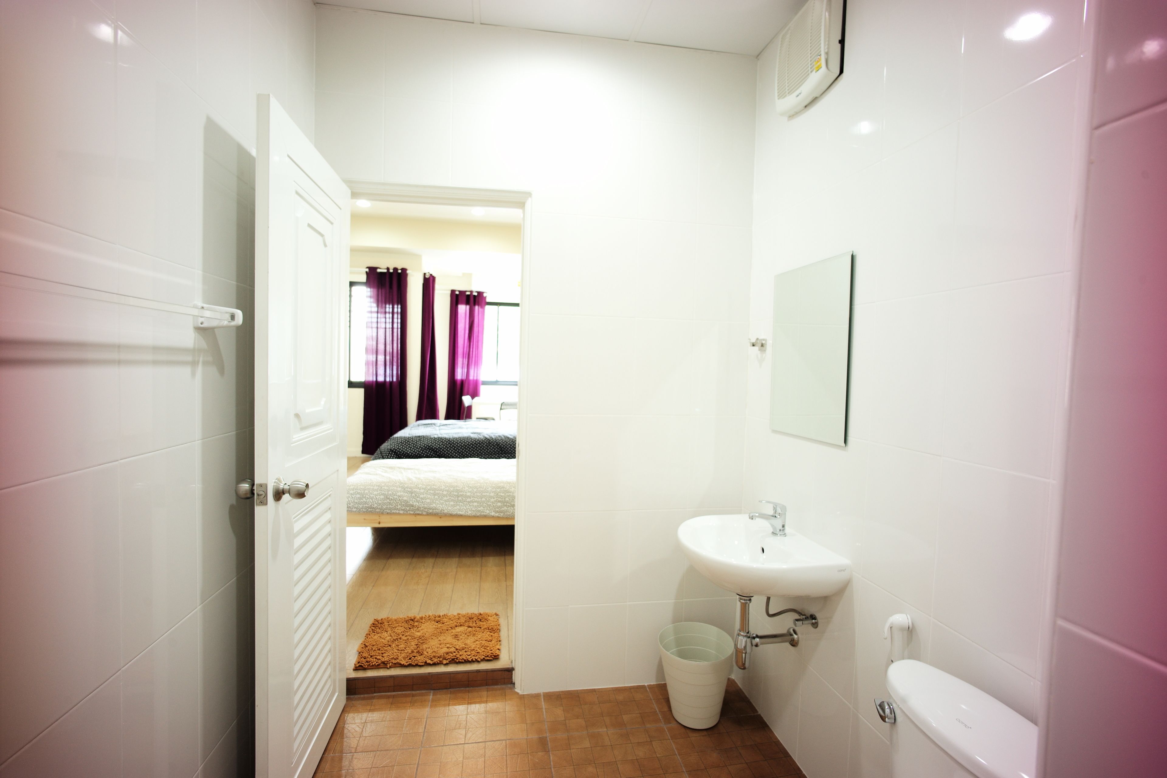 Un couloir étroit mène à une chambre à coucher équipée d’un lit et à une salle de bain avec un lavabo et des toilettes.