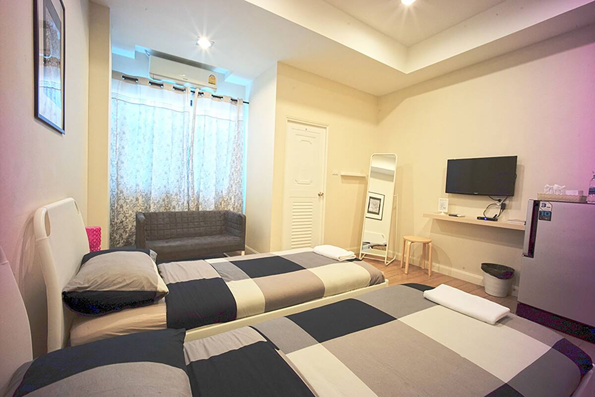 Un dormitorio con dos camas, televisión, espejo y ventana con cortinas.