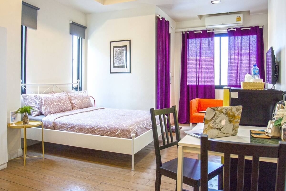 Un dormitorio con cama, escritorio, silla, ventana con cortinas y aire acondicionado de pared.