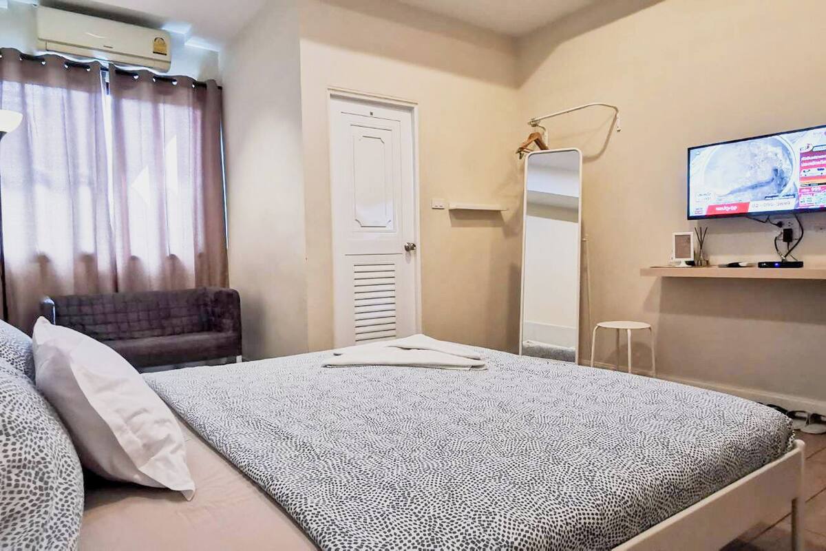 Un dormitorio con una cama, televisión, espejo, armario y una mesita.