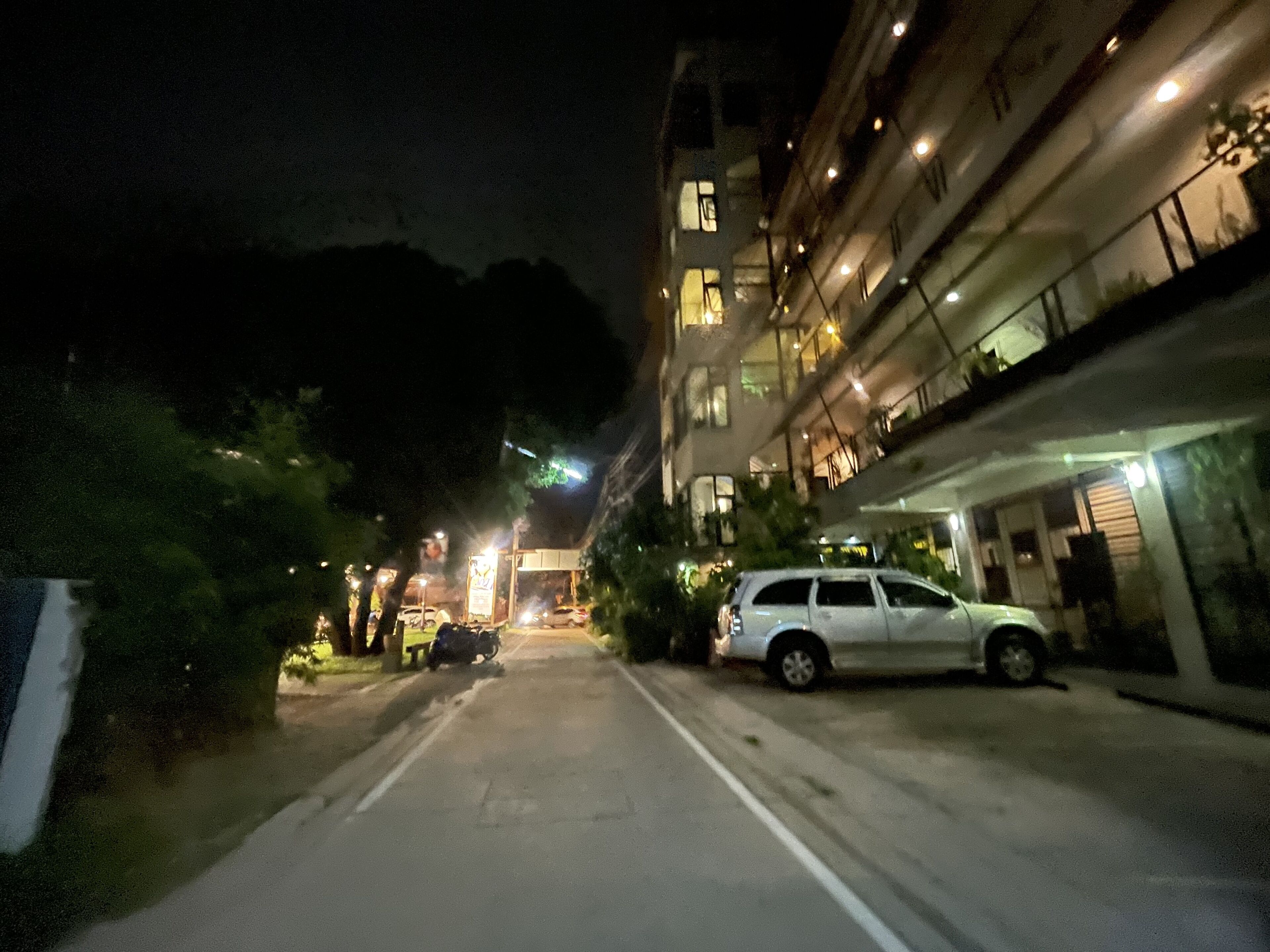 A nighttime street view with a building on the right, a parked car, and a motorcycle.