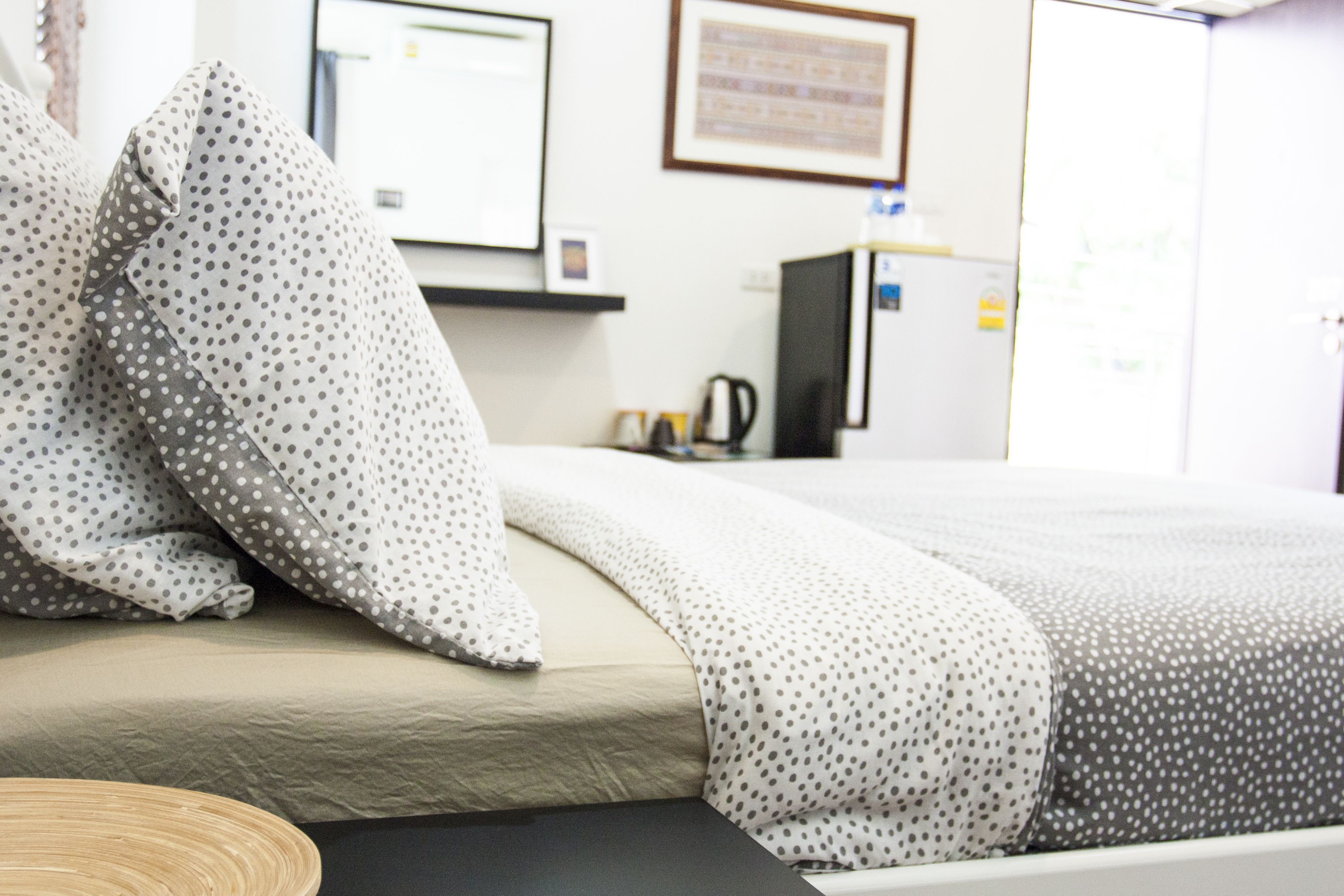A hotel room with a bed, pillows, a desk, and a refrigerator.