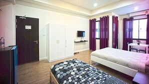 A room with a bed, a desk with a chair, a wardrobe, and a television. - 26 Bed and Coffee (Chonburi)