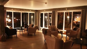 Una habitación amplia con piso de madera, varios espacios de descanso y grandes ventanales con vistas al exterior.