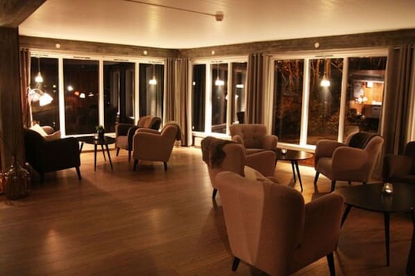 A spacious room with a wooden floor, multiple seating areas, and large windows providing a view of the outdoors.