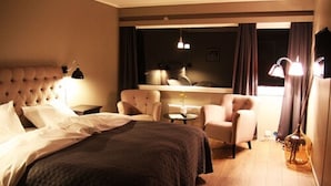 Habitación de hotel con una cama grande, un área de estar con una mesa y vista a la ciudad desde la ventana.