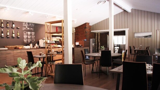 Un restaurante moderno con zona de bar, muebles de madera y un menú en una pizarra.