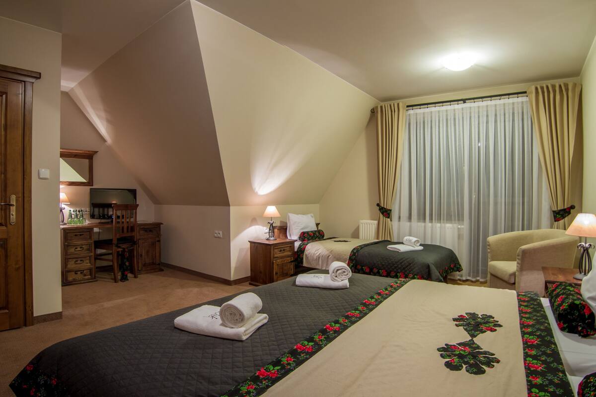 Habitación de hotel con dos camas, un escritorio con computadora, una silla y un ventanal con cortinas.