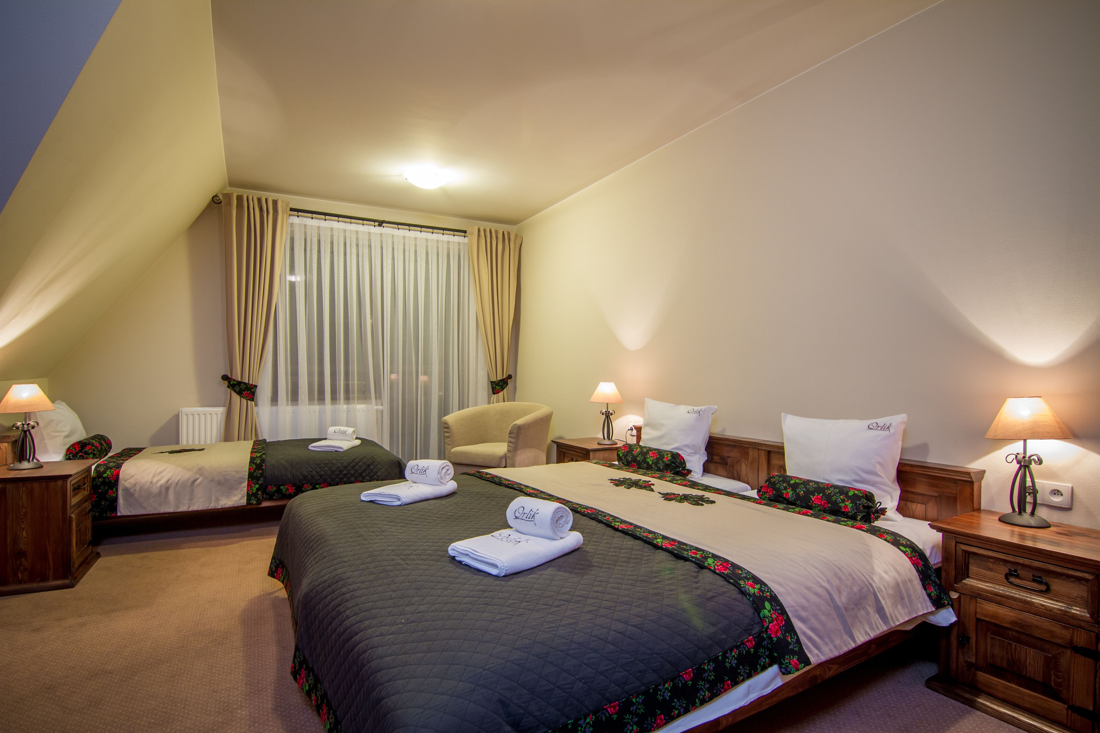 A hotel room with two beds, a chair, a nightstand, and a window with curtains.