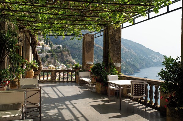 A terrace with outdoor seating, a pergola, and a view of a coastal town.