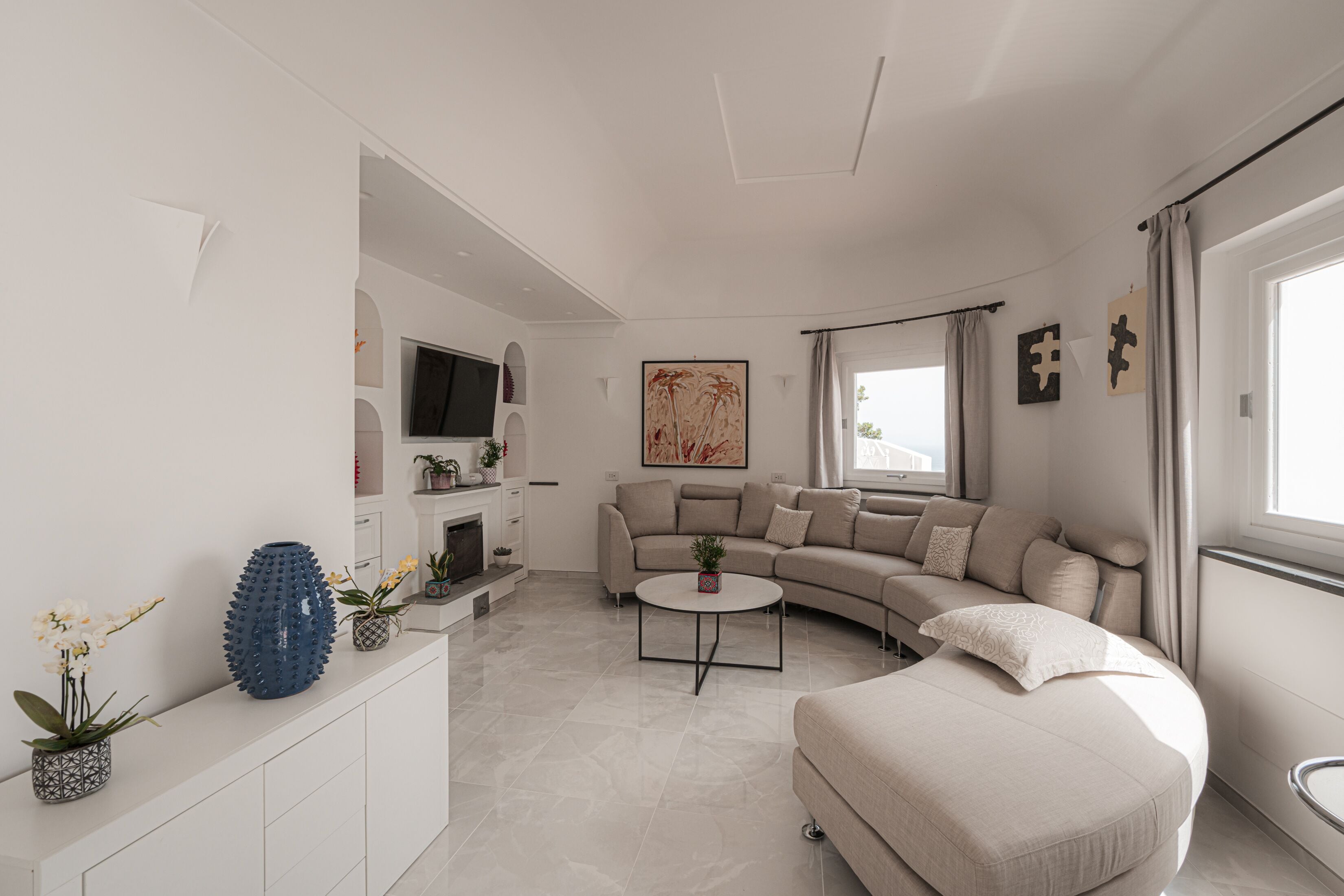 Een moderne woonkamer met een gebogen bank, een ronde salontafel en een flatscreen televisie aan de muur.