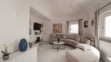 Een moderne woonkamer met een gebogen bank, een ronde salontafel en een flatscreen televisie aan de muur.
