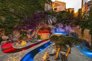 Ein angelegter Garten mit Wasserspiel, Felsformationen und einem Gebäude im Hintergrund.