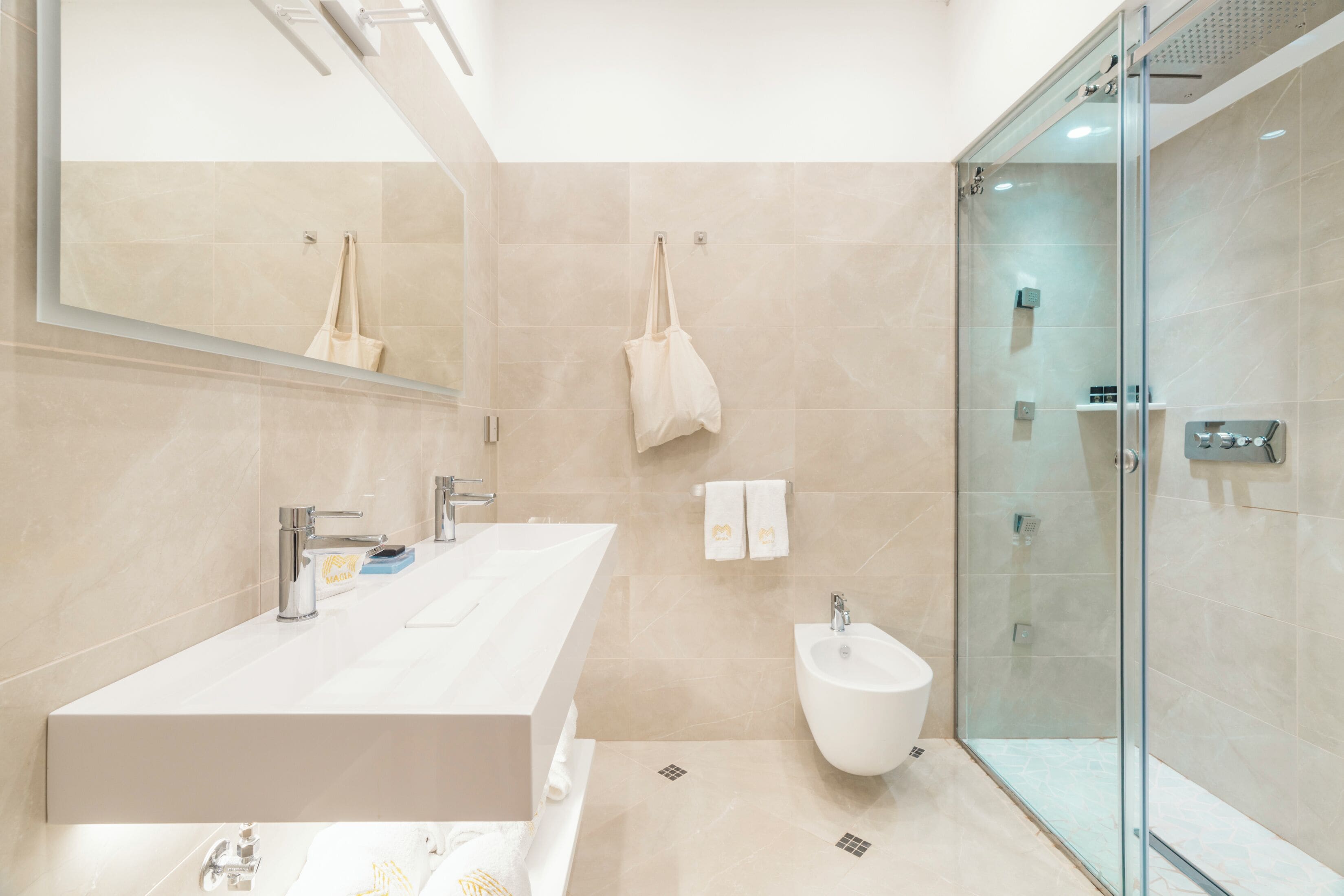 Un baño moderno con un espejo grande, un lavamanos, un bidé y una ducha con cerramiento de vidrio.