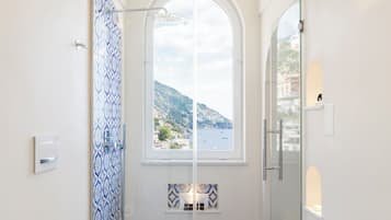 Une salle de bain équipée d’une douche, de toilettes et d’un lavabo, avec vue sur la mer par une fenêtre.