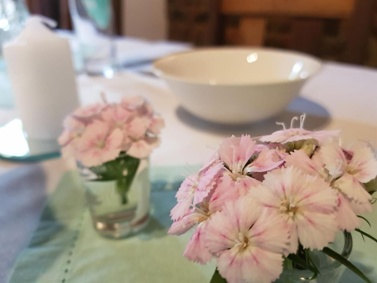 A table with a clear glass vase containing pink flowers, a white candle, and a white bowl.