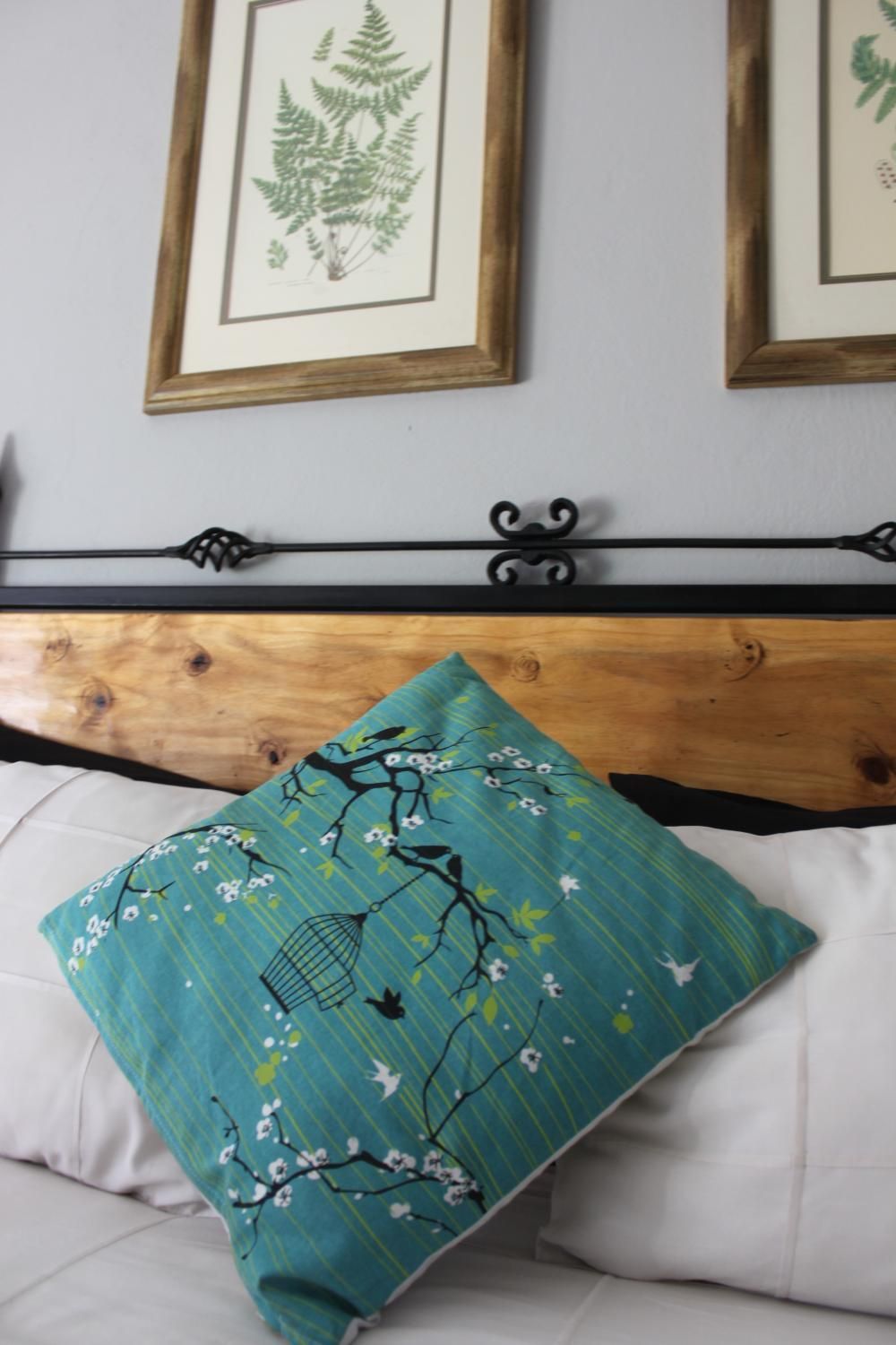 A bed with a wooden headboard, a white pillow, and a teal pillow with floral and bird designs.