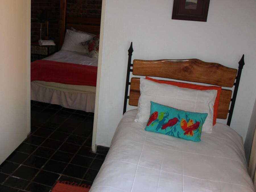 A bedroom with a wooden bed, a red blanket, and a colorful pillow.