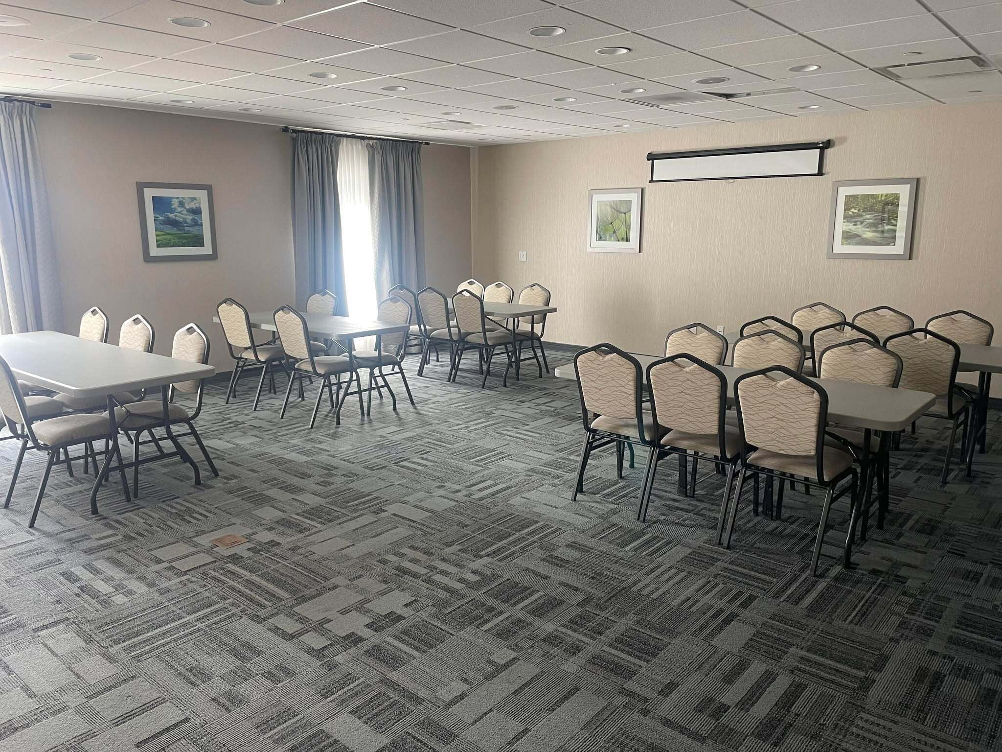 A conference room with a carpeted floor, multiple tables and chairs, and framed pictures on the walls.