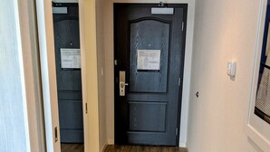 A hallway with a wooden floor, a black door with an emergency exit sign, and a small bench. - Chateau Fredericton, Trademark Collection by Wyndham (Fredericton)
