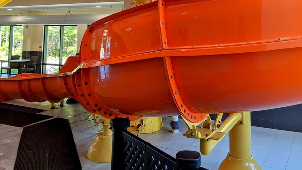 A large, orange mechanical structure with yellow supports, situated indoors with a view of greenery outside. - Chateau Fredericton, Trademark Collection by Wyndham (Fredericton)