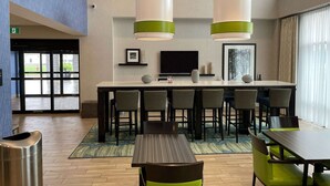 A modern hotel lobby with a central bar area, seating arrangements, and a television screen. - Chateau Fredericton, Trademark Collection by Wyndham (Fredericton)