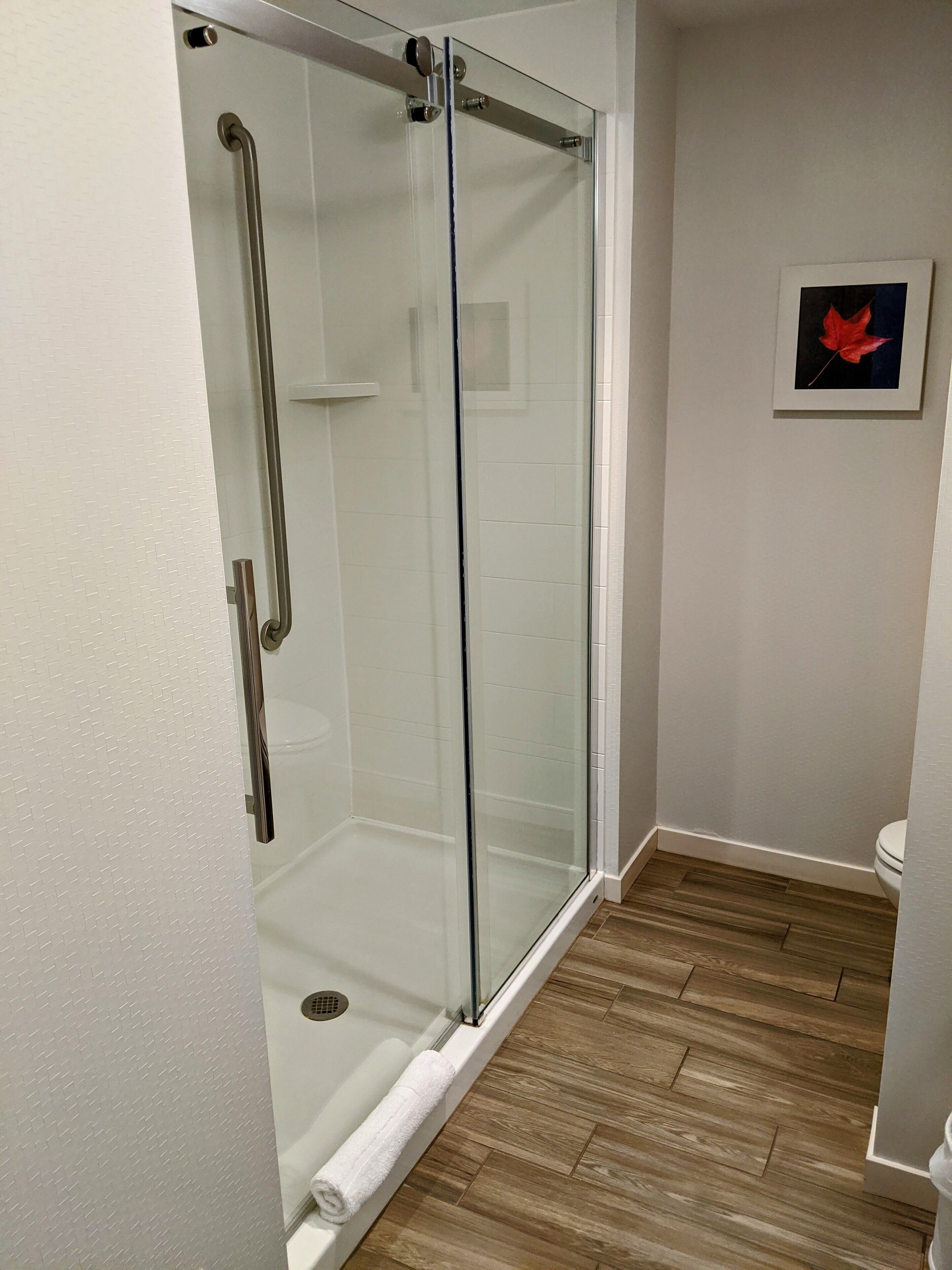 Un baño moderno con cabina de ducha de vidrio, inodoro blanco y suelo de madera.