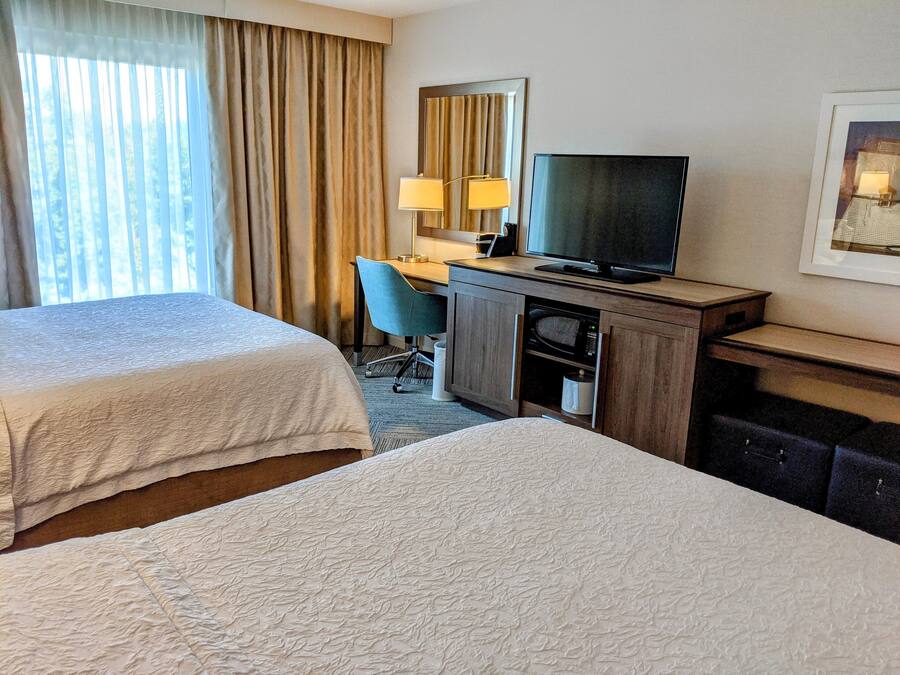 A hotel room with two beds, a desk with a computer, a television, and a microwave.