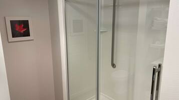 Eine Dusche mit Glastrennwand, einer Handstange, einem gerahmten Bild eines roten Blattes an der Wand und einem gefliesten Duschbereich.