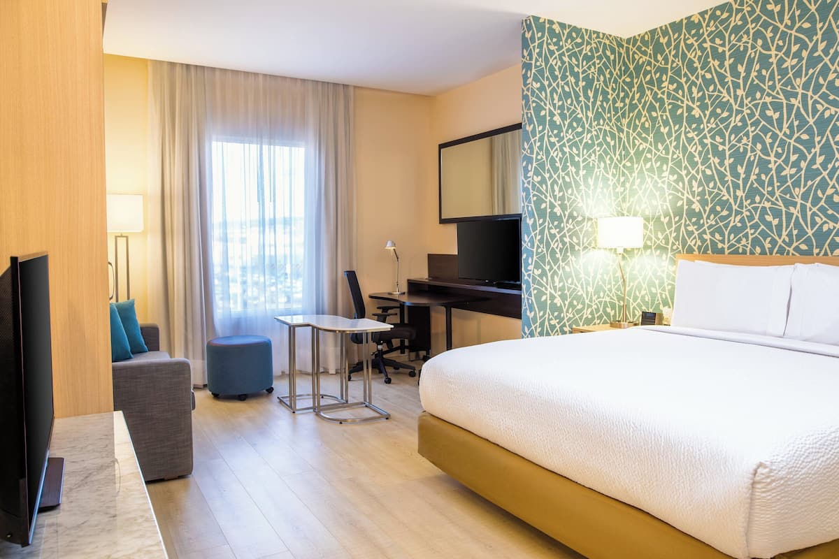 A hotel room with a large bed, a desk, a chair, a television, and a window with curtains.