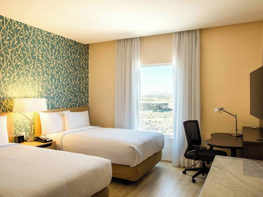 Habitación de hotel con dos camas, un escritorio, una silla, un televisor y una ventana con vistas.