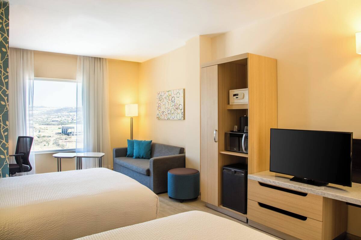 A hotel room with two beds, a sofa, a TV, a desk, and a view of the city.